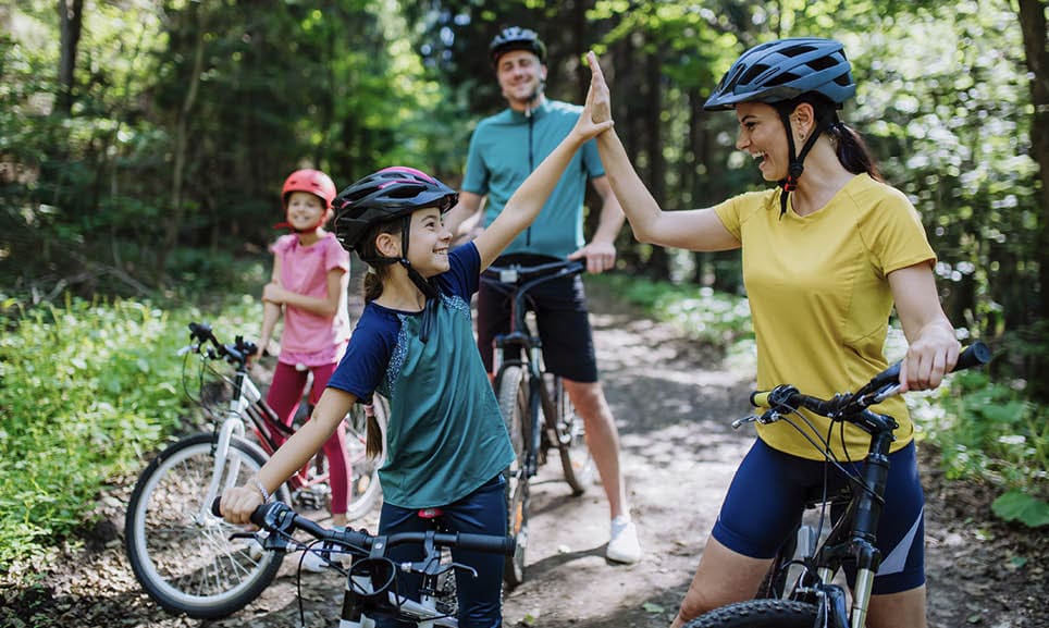A young family with little children preapring for bike ride, standing with bicycles in nature and high fiving.
